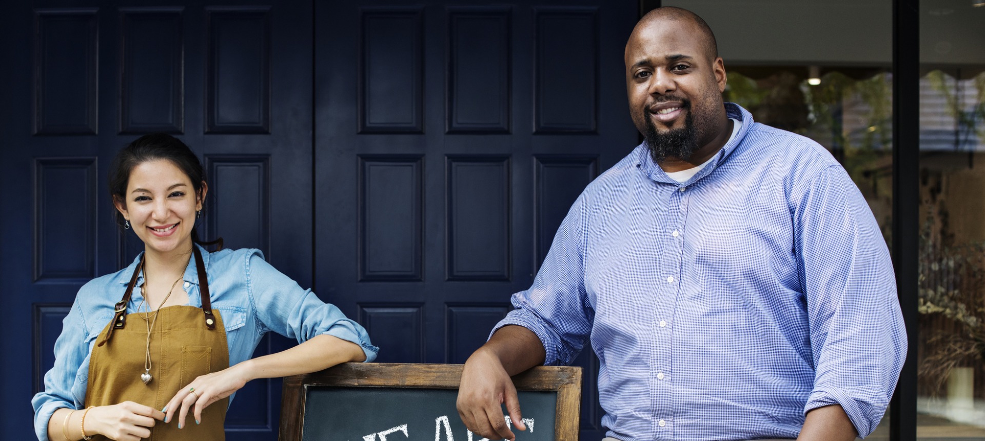 Cheerful business owners standing with open blackboard