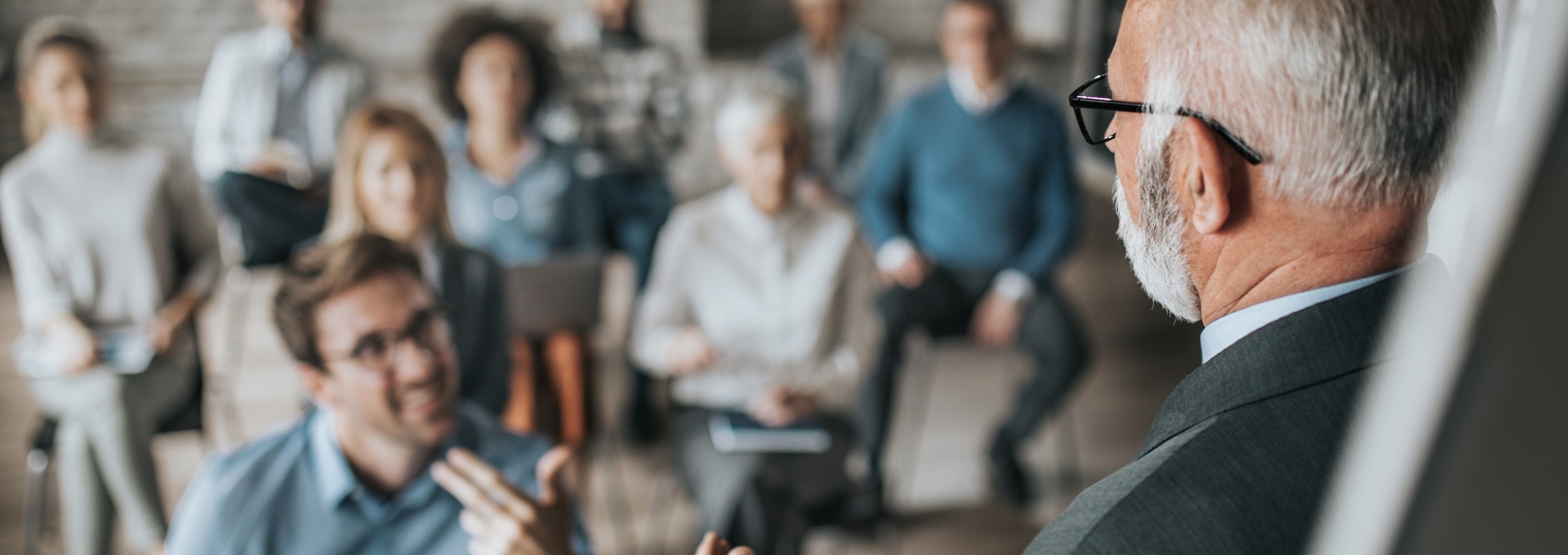 Mature public speaker giving a presentation to large group of business people in a board room