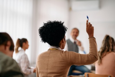 Back view of African American student raising her arm to answer a question during lecture in the classroom.