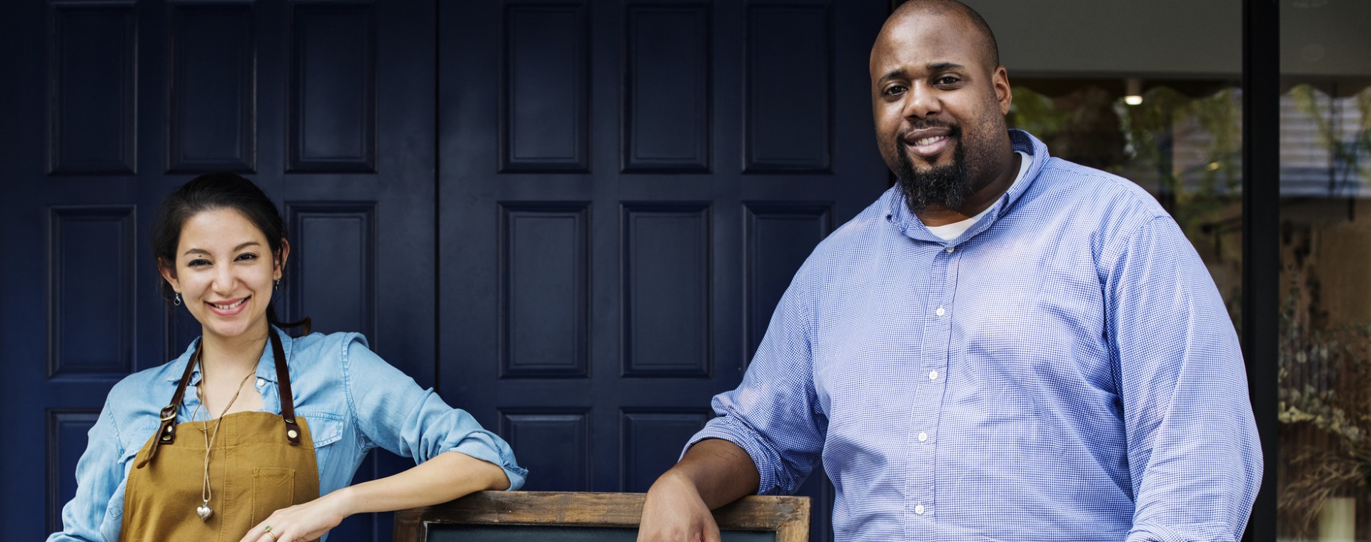 Cheerful business owners standing with open blackboard