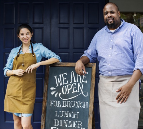 Cheerful business owners standing with open blackboard